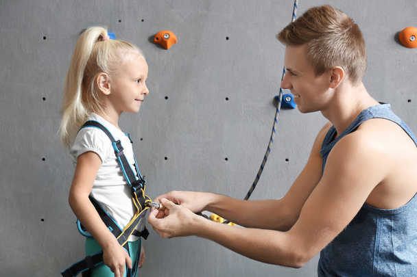 Instructor putting harness on little girl in climbing gym - Foto, imagen