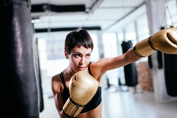 young woman with serious look in yellow sparring gloves fighting indoors - Valokuva, kuva