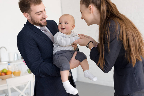 smiling business parents in formal wear holding baby at home - Fotó, kép