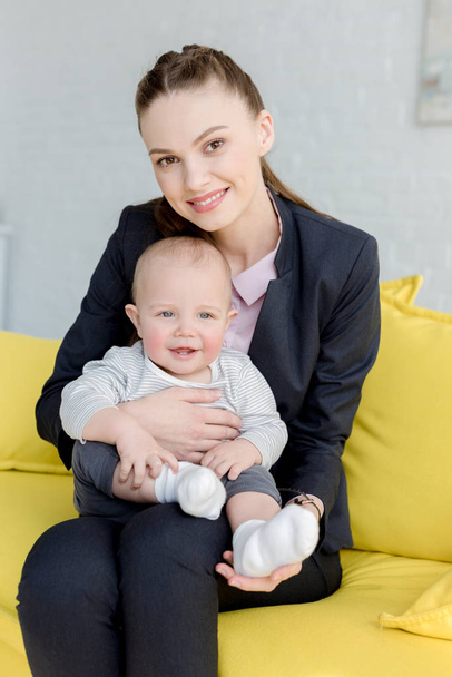 beautiful smiling businesswoman sitting on sofa with little son - Zdjęcie, obraz