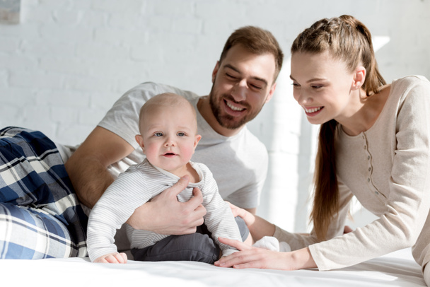 happy parents with little son on bed - Foto, afbeelding