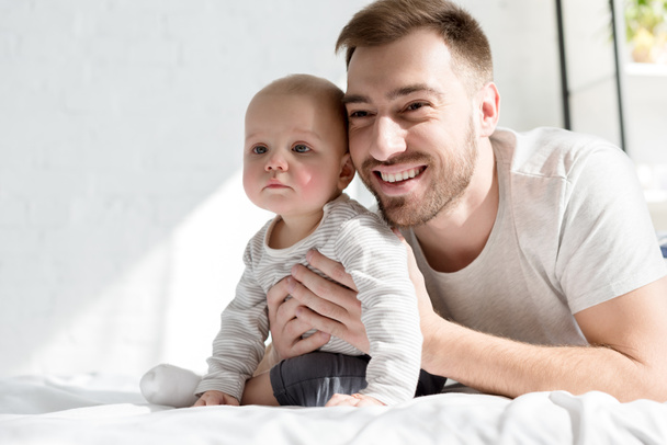 yatakta yatarken küçük oğlu ile gülümseyen yakışıklı baba - Fotoğraf, Görsel