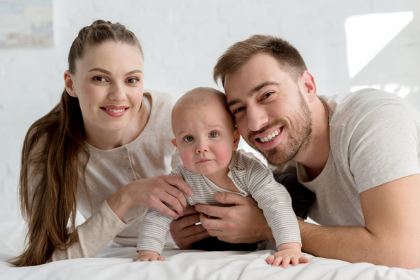 smiling parents with little boy on bed - Fotografie, Obrázek