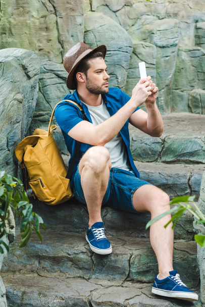 komea nuori mies ottaa valokuvan älypuhelimella istuessaan kiviportaissa
 - Valokuva, kuva