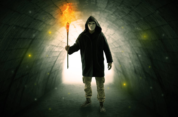 Mann läuft mit brennendem Flambeau durch dunklen Tunnel - Foto, Bild