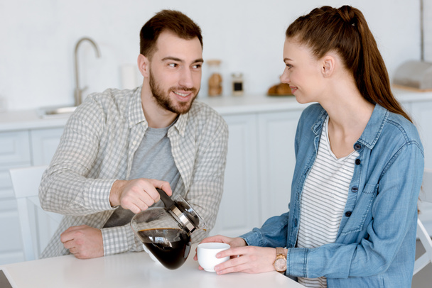 boyfriend pouring coffee for girlfriend in kitchen - Fotografie, Obrázek