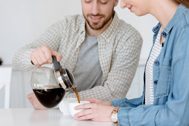 aviomies kaatamalla kahvia potin kuppeja keittiössä vaimonsa kanssa
 - Valokuva, kuva