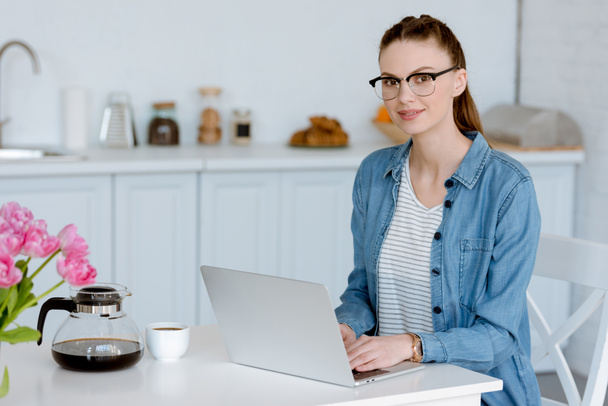 teletrabajo femenino joven con café usando portátil en la cocina
  - Foto, Imagen