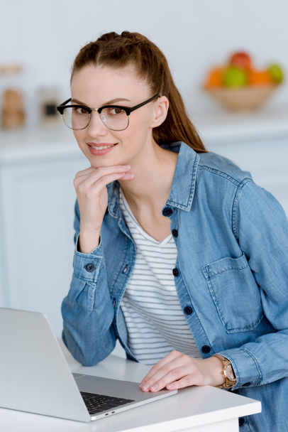 young female freelancer working with laptop on kitchen  - Фото, изображение