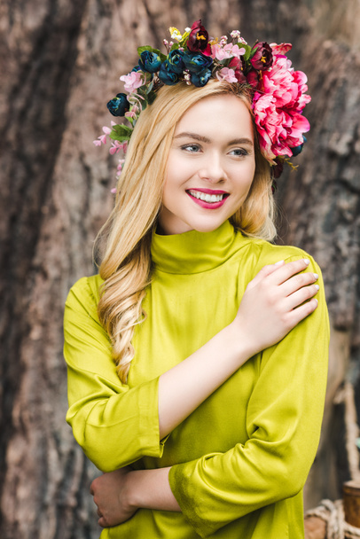 happy young woman with floral wreath with blurred tree trunk on background - Foto, Imagem