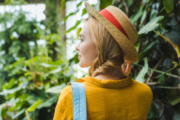 rear view of beautiful young woman in straw hat surrounded with tropical plants - Фото, зображення