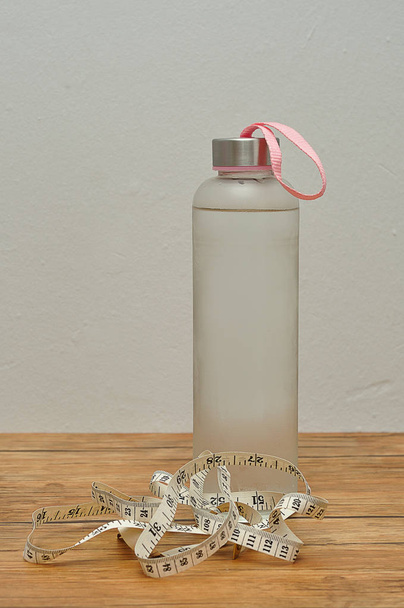 A glass bottle filled with ice cold water and a measuring tape - Photo, Image