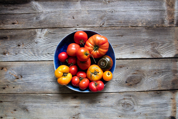plate of different heirloom colorful tomatoes on beautiful old wooden table for genuine organic mediterranean diet and earthy gardening, copy space, top view - Fotografie, Obrázek