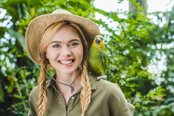 happy young woman in safari suit with parrot on shoulder in jungle - Foto, immagini