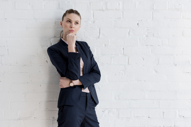 beautiful thoughtful businesswoman in suit posing near white wall  - Φωτογραφία, εικόνα