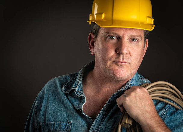 Серьезный подрядчик в жесткой шляпе, держащий удлинитель с драмой
 - Фото, изображение
