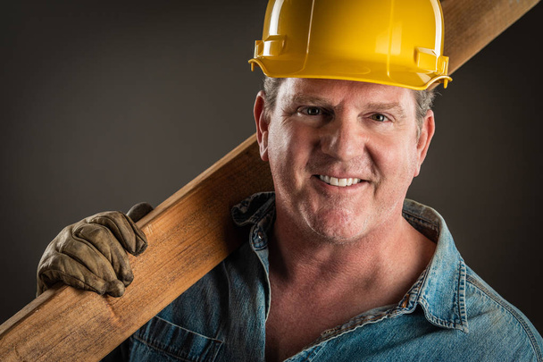 Entrepreneur souriant dans Hard Hat tenant la planche de bois avec éclairage dramatique
. - Photo, image