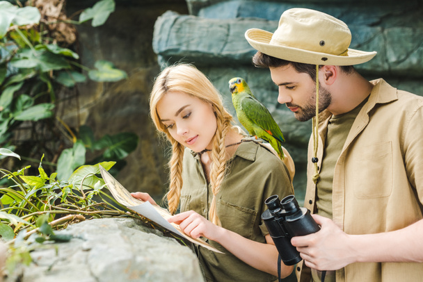 attractive young couple in safari suits with parrot trying to navigate in jungle - Photo, Image