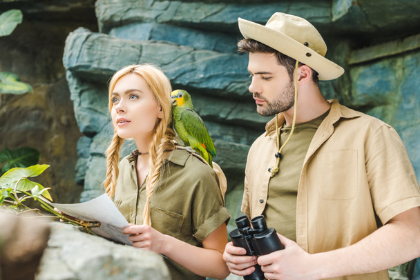 hermosa pareja joven en trajes de safari con loro tratando de navegar en la selva
 - Foto, Imagen