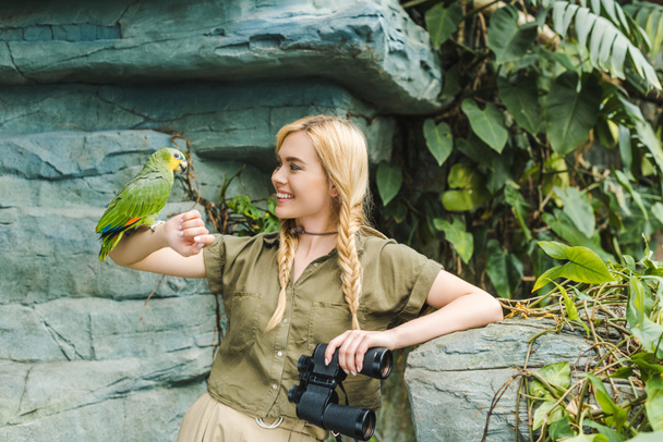 приваблива молода жінка в сафарі-костюмі з папугою, що вбирається на руку в джунглях
 - Фото, зображення