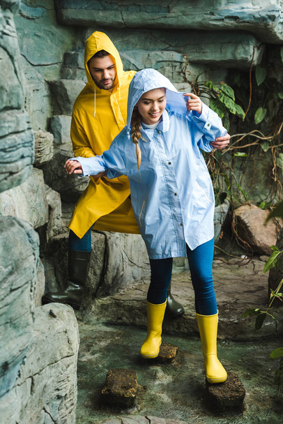happy young couple in raincoats walking by jungle - Photo, image