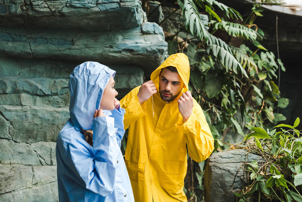 attractive young couple in raincoats in jungle - Фото, изображение