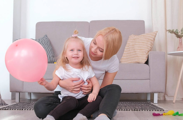 attraktive junge blonde Mutter und ihre charmante Tochter spielen zusammen mit rosa Ballon. - Foto, Bild