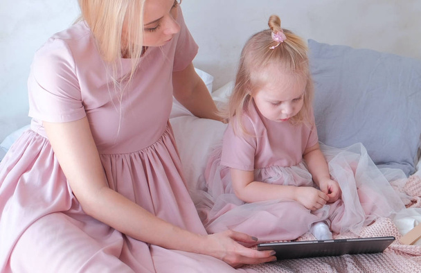Viehättävä pieni vaalea tyttö katsomassa videota tabletilla äitinsä kanssa
 - Valokuva, kuva