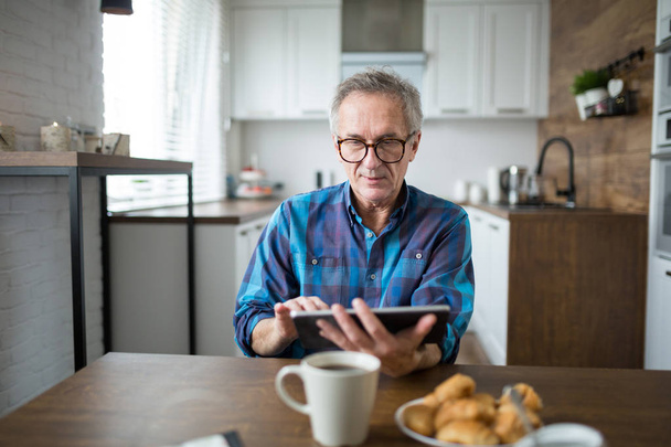 Senior man using tablet at kitchen table - Photo, image