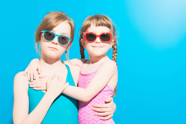 Meninas bonitas em roupa de banho com óculos abraçando no fundo azul
 - Foto, Imagem