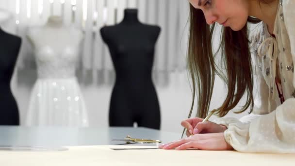 Krásná dívka módní návrhář nakreslí na papírové šablony k vyřezávání tkaniny na figuríny oblečené do svatebních šatů. Výrobce svatebních šatů. - Záběry, video