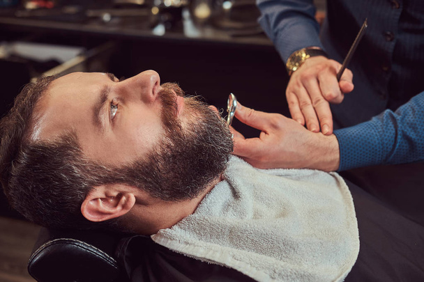 Cabeleireiro profissional modelando barba com tesoura e pente na barbearia. Foto de close-up
. - Foto, Imagem