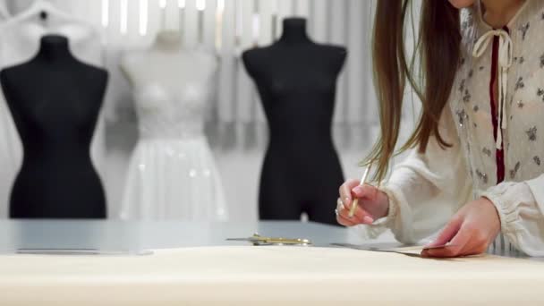 Mooie modeontwerper meisje op papier met uitgesneden gouden schaar patronen voor weefsel op de achtergrond van de mannequins gekleed in trouwjurken. Fabrikant van trouwjurken. - Video