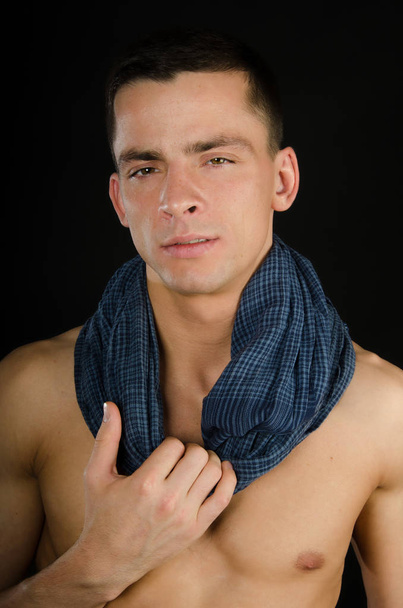 Sexy jongeman met een mooi lichaam in een sjaal. Model met atletisch lichaam poseren op een zwarte achtergrond. Jonge aantrekkelijke kerel. Naakt en sexy - Foto, afbeelding