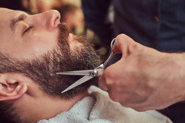 Peluquería profesional modelando barba con tijeras y peine en la barbería. Foto de primer plano
. - Foto, imagen