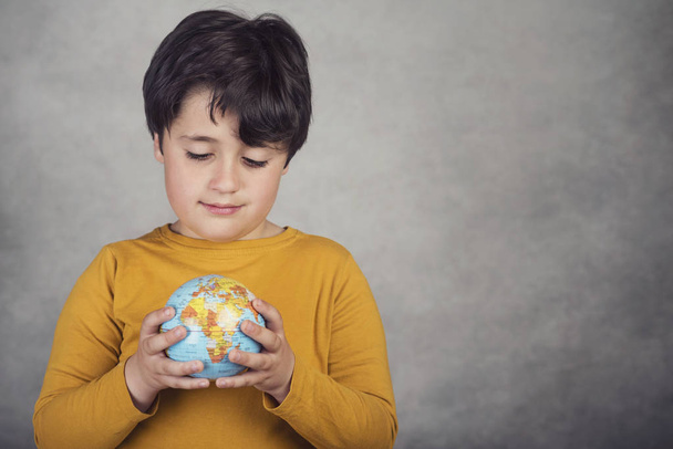 lachende jongen met een earth globe op grijze achtergrond - Foto, afbeelding