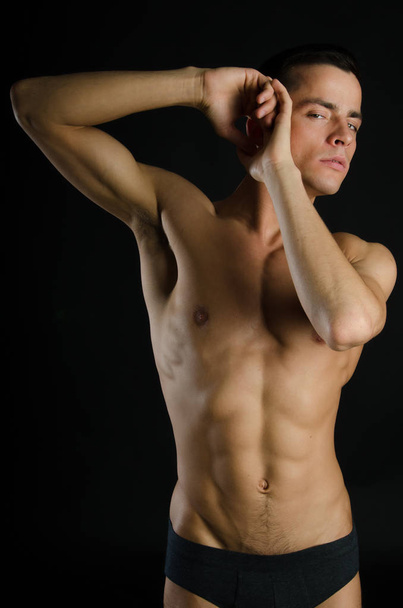 Young sexy man with a beautiful body. Model with athletic body posing on a black background. Young attractive guy. - Zdjęcie, obraz