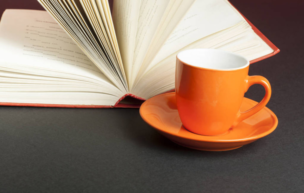 Κούπα για τσάι ή καφέ και ανοιχτό βιβλίο σε μαύρο φόντο. Έννοια της εκπαίδευσης. - Φωτογραφία, εικόνα