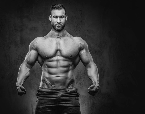 Portrait of a shirtless tall huge male with a muscular body with a stylish haircut and beard, in a sports shorts, posing in a studio. Isolated on a dark background. - Photo, Image
