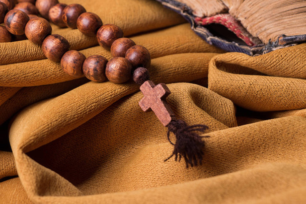 Croce cristiana in legno e rosario e vecchia bibbia su uno sfondo di drappeggio in tessuto dorato. Libro sacro
. - Foto, immagini