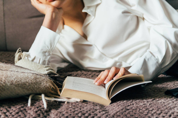 girl reading a book in a warm blanket. woman lies, lay down on the bed, a blanket, a sofa, a couch and holds a book. Girl reading a book - Photo, image