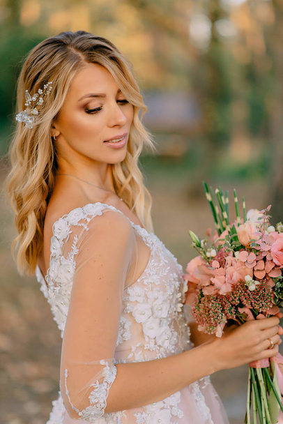 beautiful bride stands with a bouquet in hands on a nature background - Foto, afbeelding
