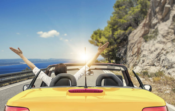 Jeune femme dans une voiture sur la route de la mer dans un contexte de belles montagnes par une journée ensoleillée
. - Photo, image
