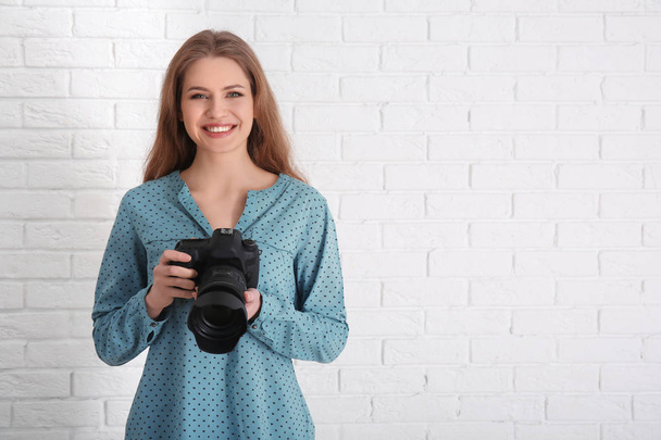 Female photographer with camera on brick background - Foto, afbeelding