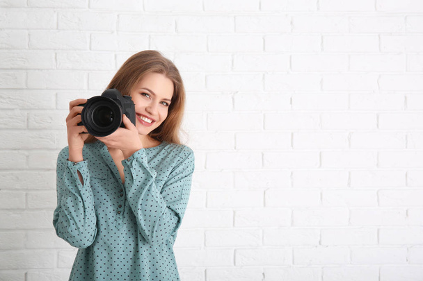 Female photographer with camera on brick background - Fotó, kép