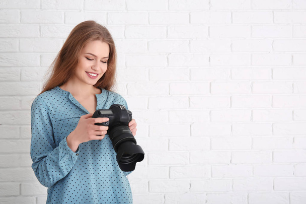 Female photographer with camera on brick background - Zdjęcie, obraz
