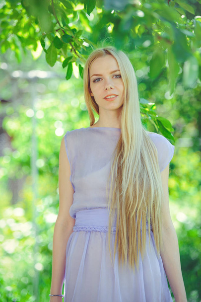 attraktive bescheidene junge Mädchen mit blonden Haaren und natürlichem Make-up in lila Kleid im Freien, Zärtlichkeit und Weichheit auf Naturhintergrund - Foto, Bild