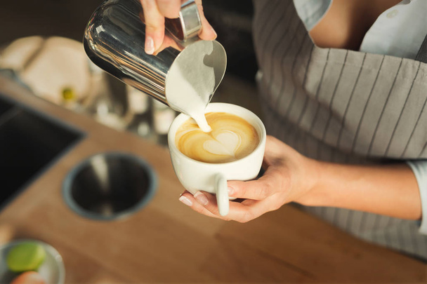 Closeup of barmen pouring milk to cappuccino cup - Foto, afbeelding