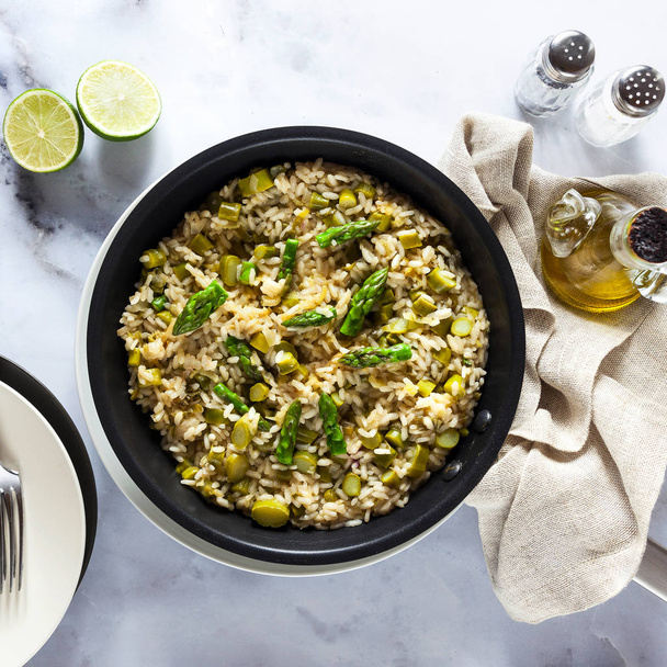 risotto with asparagus in a frying pan on a white marble table.  - Photo, Image