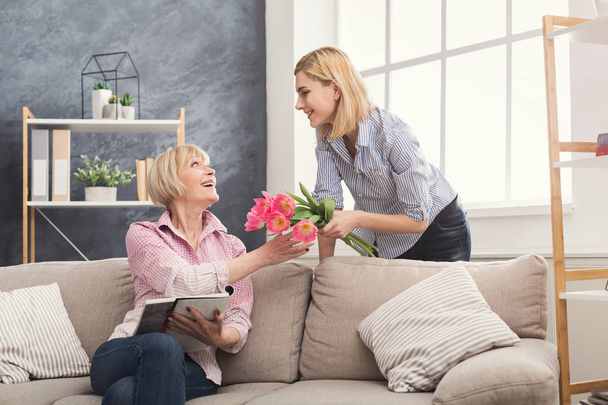 Daughter giving flowers to adult mother - Foto, afbeelding